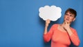 Studio shot of a young woman with a puzzled expression, holding a white empty banner in the form of a cloud on a blue Royalty Free Stock Photo