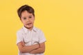 Studio portrait of a little smiling blond boy wearing white shirt with arms crossed on a yellow background Royalty Free Stock Photo