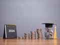 Study goals, 2024 Desk calendar, Glass bottle with graduation hat and stack of coins. The concept of saving money for education, Royalty Free Stock Photo