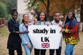 Study in UK. Group of five african college students on campus at university yard hold white blank. Abroad countries for student