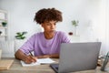 Studying from home concept. Serious black teen guy taking notes while participating in online lesson on laptop Royalty Free Stock Photo