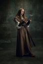 Vintage portrait of young beautiful girl in image of medieval warlike woman using modern gadget isolated over dark