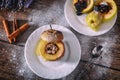 Stuffed baked apple with nuts, honey and chocolate on white dessert plates, dark wooden background. Christmas sweet