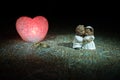 Stuffed bride and groom bears standing together with LED heart on dark foggy background.