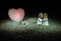 Stuffed bride and groom bears standing together with LED heart on dark foggy background.