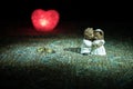 Stuffed bride and groom bears standing together with LED heart on dark foggy background.