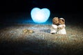 Stuffed bride and groom bears standing together with LED heart on dark foggy background.