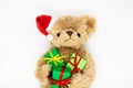 A stuffed toy Teddy bear in a red Santa Claus hat with a pompom on one ear, holding green gift boxes in its paws. White background Royalty Free Stock Photo