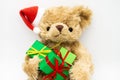 A stuffed toy Teddy bear in a red Santa Claus hat with a pompom on one ear, holding green gift boxes in its paws. White background Royalty Free Stock Photo