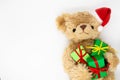 A stuffed toy Teddy bear in a red Santa Claus hat with a pompom on one ear, holding green gift boxes in its paws. White background Royalty Free Stock Photo