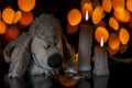 A stuffed white colored dog toy with some wax candles with it on wooden surface with blurred bokeh background of Christmas lights.