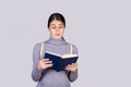 Stunned emotive young woman looking amazed in a book, found a shocking text. Surprised student girl reader holding a red textbook Royalty Free Stock Photo