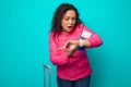 Stunned Hispanic woman in bright pink jacket looks at her watch with surprise and fear, being late for her flight, holding