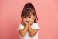 Stunned little three years old asian girl keeps hands on cheeks from wonder standing in white t shirt isolated over pink