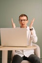 Stunned male furiously raise hands while working on laptop at table. Man in glasses bemused by result, look at monitor. Royalty Free Stock Photo