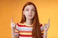 Stunned thrilled young redhead woman peer focused pointing up index fingers upwards look concentrated excited hold