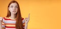 Stunned thrilled young redhead woman peer focused pointing up index fingers upwards look concentrated excited hold