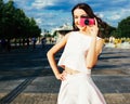 A stunning Asian girl in summer bright outfit posing on the street with a pink vintage camera taking a picture