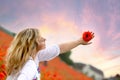 Stunning background of the sunset sky and a woman`s hand with a red poppy flower