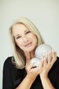 Stunning beautiful and self confident best aged woman with grey hair smiling into camera, holding Christmas decoration baubles