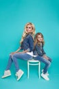 Stunning beauty of a young mother with a cute blonde daughter sitting on a chair on a blue background dressed Royalty Free Stock Photo