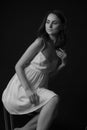 Stunning black and white portrait of a sexy young brunette girl in a white midi dress sitting on a high chair on a black backgroun Royalty Free Stock Photo