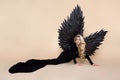 Stunning blonde woman in elegant long black dress and big wings is posing in studio. Luxury evening fashion. Glamour fashion model Royalty Free Stock Photo