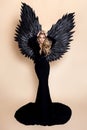 Stunning blonde woman in elegant long black dress and big wings is posing in studio. Luxury evening fashion. Glamour fashion model Royalty Free Stock Photo