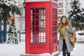 Stunning brunette woman in yellow cardigan standing near british call-box in winter day. Outdoor photo of adorable girl