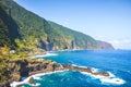 Stunning cliffs on the northern coast of Madeira Island, Portugal. Steep green rocks, small city and dark blue sea water