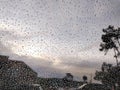 Stunning closeup of rain droplets on a window, creating a mesmerizing abstract texture against a blurred cityscape and cloudy sky