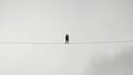 A Man Walking on a Tightrope in a White Sky Background (Balance, Equilibrium, Resilience, Difficult Situation Metaphor) Royalty Free Stock Photo