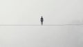 A Man Walking on a Tightrope in a White Background (Balance, Equilibrium, Resilience, Difficult Situation Metaphor) Royalty Free Stock Photo