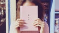 A Girl Holding a Pink Book Covering Her Face in Pastel Colors Royalty Free Stock Photo
