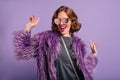 Stunning cute girl with curly brown hair posing with pleasure on purple background. Indoor photo of dancing young lady Royalty Free Stock Photo