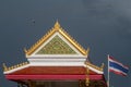 Stunning detail of a Buddhist temple with the Thai flag blowing in the wind, against a black sky full of rain, Bangkok, Thailand