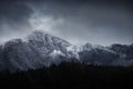 Stunning dramatic landscape image of snowcapped Glyders mountain range in Snowdonia during Winter with menacing low clouds hanging