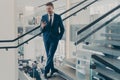 Stunning entrepreneur in formal stylish suit standing on staircase in office lobby with smartphone Royalty Free Stock Photo