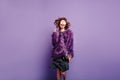 Stunning girl in good mood jumping on purple background and smiling. Studio shot of spectacular woman in fluffy winter