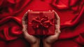 Gift of Love: Woman\'s hands holding luxury box with bow in top down view against a vibrant red backdrop