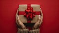 Gift of Love: Woman\'s hands holding luxury box with bow in top down view against a vibrant red backdrop