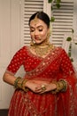 Stunning Indian bride adorned in a traditional red bridal lehenga gracefully wears heavy gold jewelry Royalty Free Stock Photo