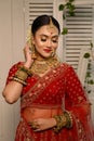 Stunning Indian bride adorned in a traditional red bridal lehenga gracefully wears heavy gold jewelry Royalty Free Stock Photo