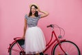 Stunning latin girl in lush skirt standing near red bicycle. Adorable woman in trendy clothes posin