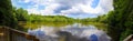 A stunning panoramic shot of the vast lake water with lush green trees and plants reflecting off the lake with blue sky and clouds Royalty Free Stock Photo