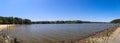 A stunning panoramic shot of the vast rippling green waters of a lake surrounded by lush green trees with clear blue sky