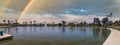 A stunning panoramic shot of a vast rippling lake surrounded by lush green palm trees, grass and plants with blue sky, clouds