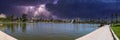 A stunning panoramic shot of a vast rippling lake surrounded by lush green palm trees, grass and plants with powerful storm clouds Royalty Free Stock Photo