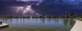 A stunning panoramic shot of a vast rippling lake surrounded by lush green palm trees, grass and plants with powerful storm clouds Royalty Free Stock Photo