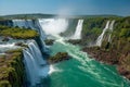 Stunning panoramic view of a powerful waterfall cascading through lush green cliffs into turquoise river waters under a clear blue Royalty Free Stock Photo